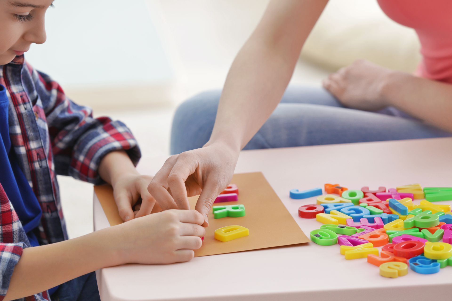 Boy using colorful letters with a person at a table, learning.