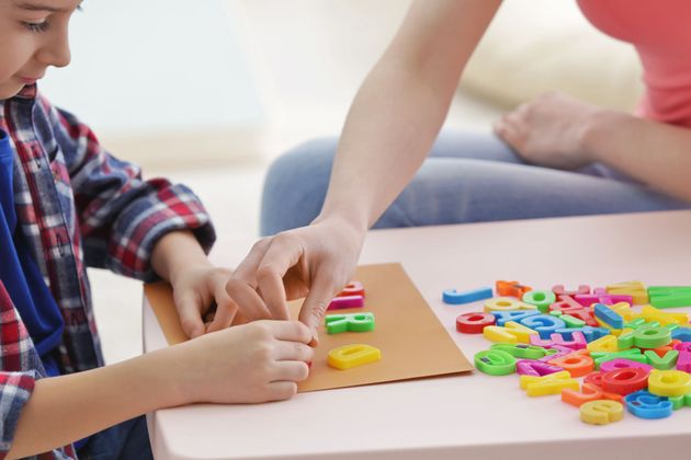 Boy and adult playing with colorful letter magnets on a table.