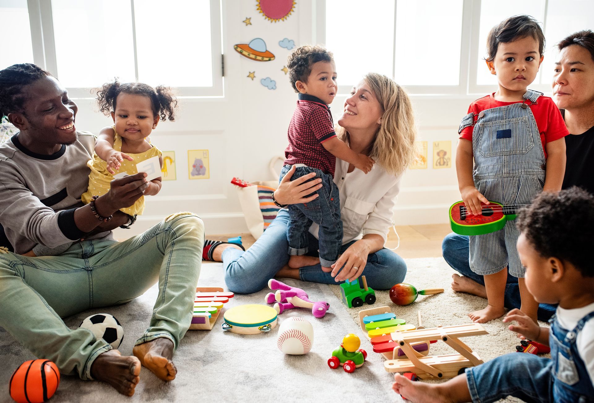 Adults and children in a brightly lit playroom. Adults interacting with children who are playing with toys.