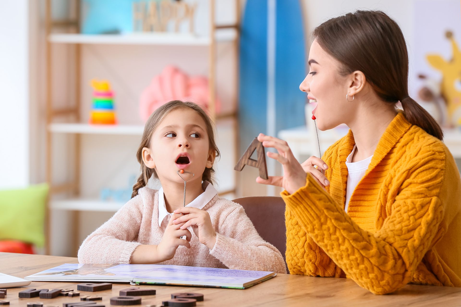 A speech therapist helping a child practice pronunciation. The therapist holds a letter 