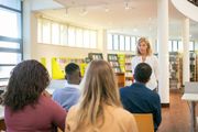 Woman lecturing to a small group of students in a library.