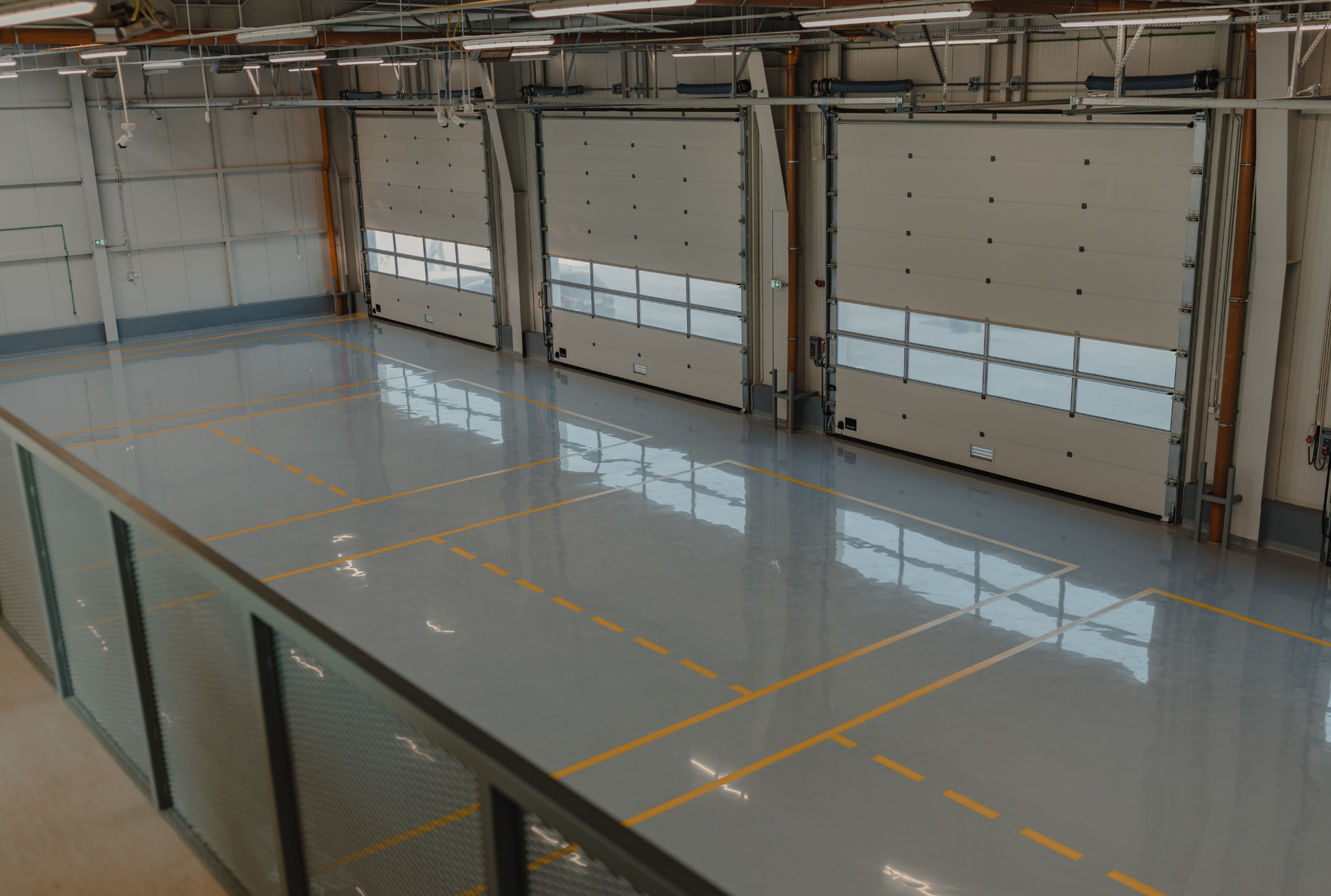 Empty industrial warehouse with large doors and a reflective gray floor.