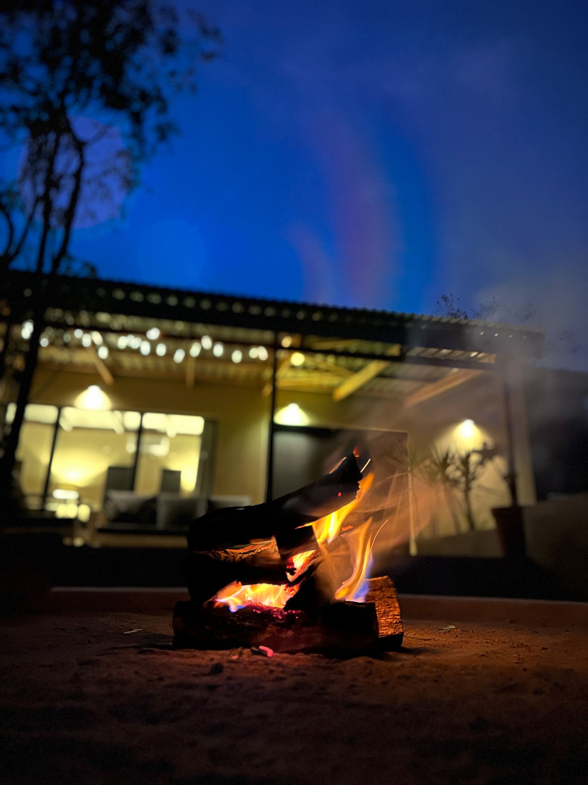 A fire pit is lit up in front of a house at night.