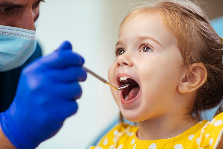 Dentist and assistant smile with a young boy in dental chair, blue scrubs and room.