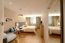 Modern hotel room with a bed, sofa, desk, and a large mirror reflecting the space.