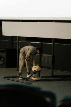 Person in a jumpsuit vacuums a dark room with a large screen.