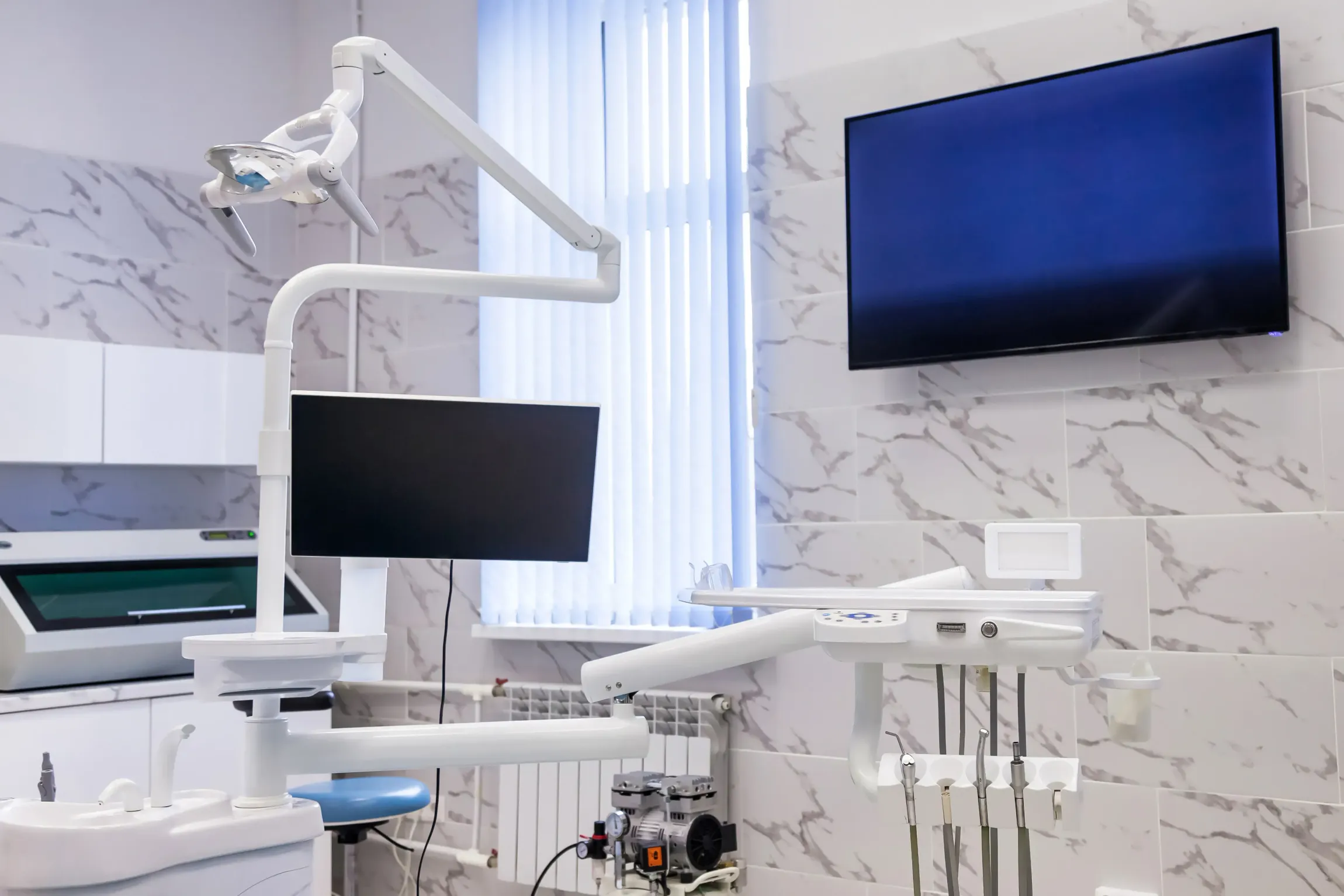 A dental office with a dental chair and a television on the wall.