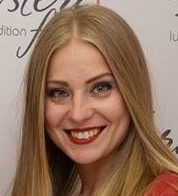 A woman with long blonde hair is smiling and wearing red lipstick.