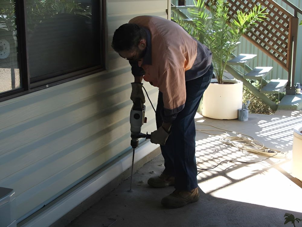 A Man is Using a Hammer to Drill a Hole in a Wall — Audy Geiszler Pest Control in Bowen, QLD