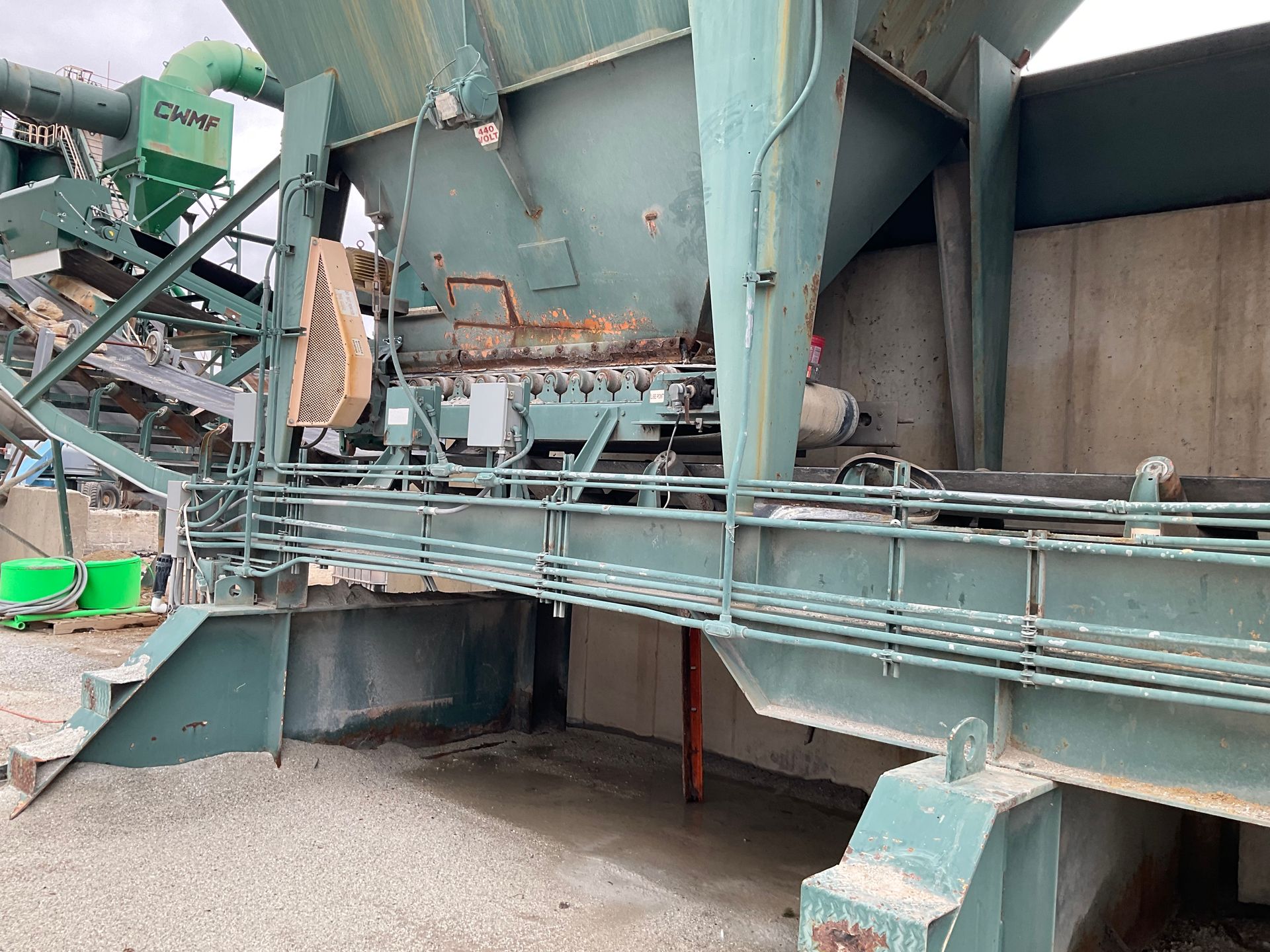 A large green machine is sitting on top of a gravel field.
