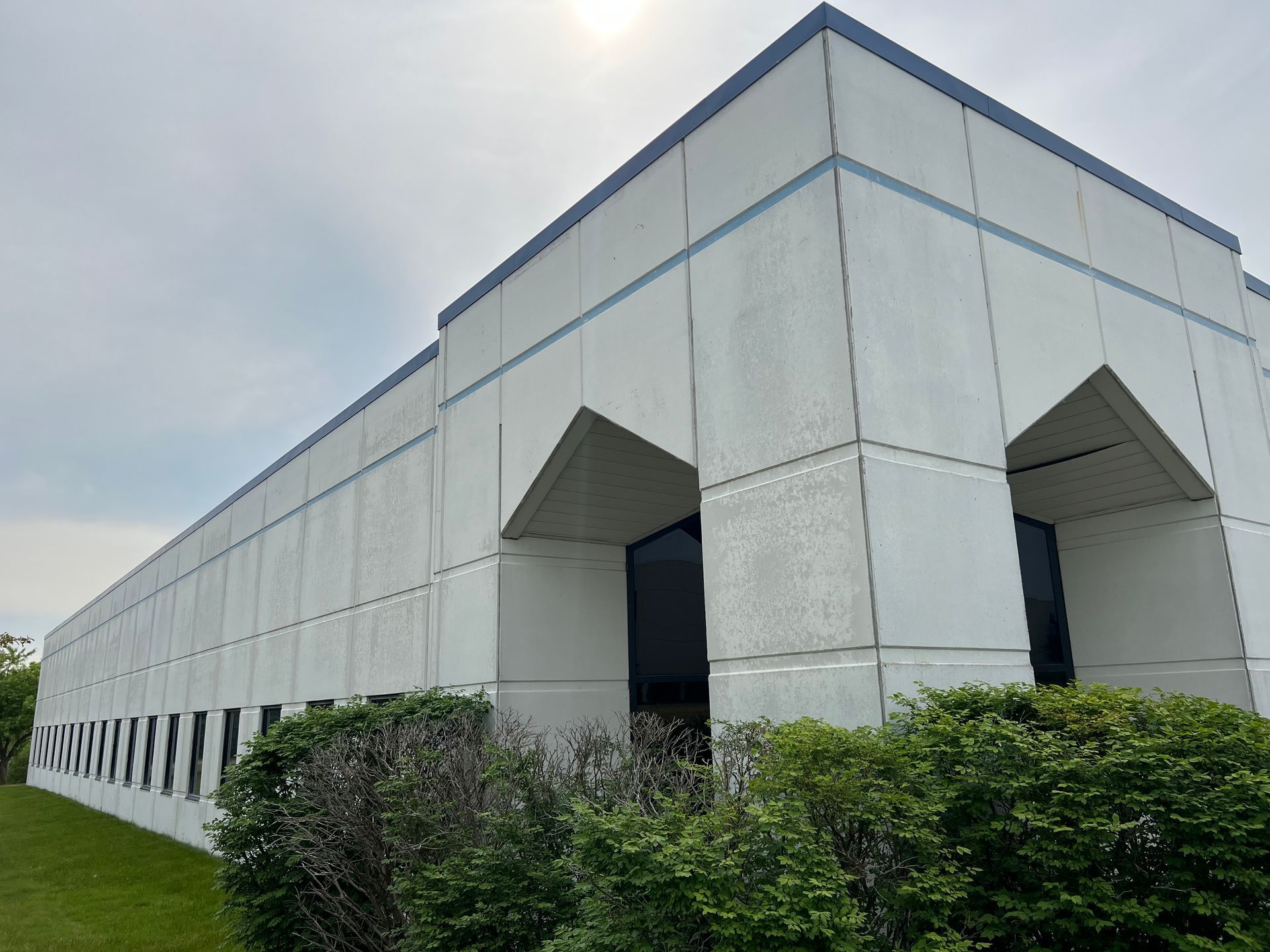 A large white building with a blue trim is surrounded by trees and grass.