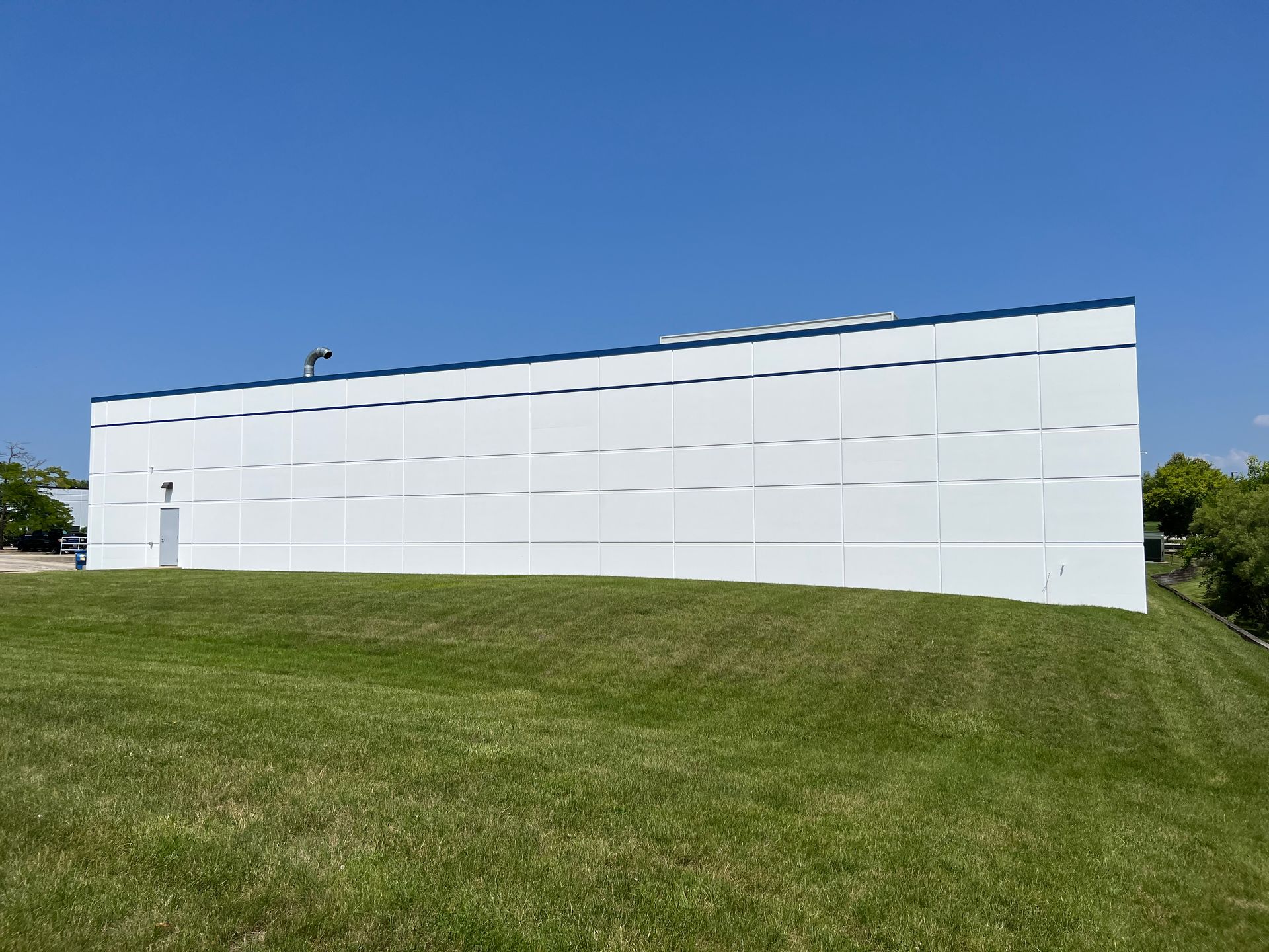 A large white building is sitting on top of a grassy hill.