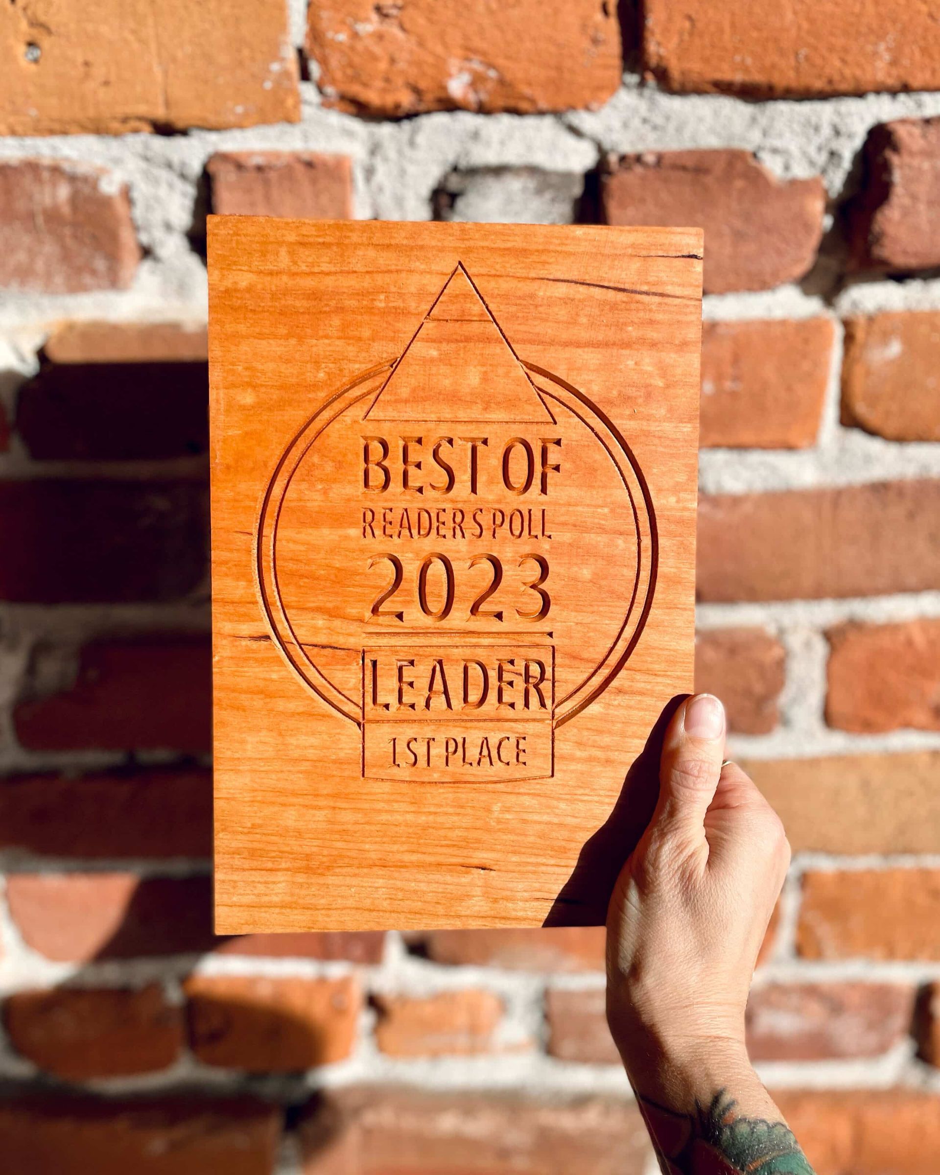 A person is holding a wooden sign in front of a brick wall.