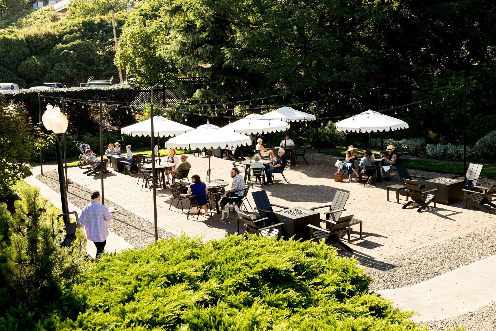 A group of people are sitting at tables under umbrellas in a park.