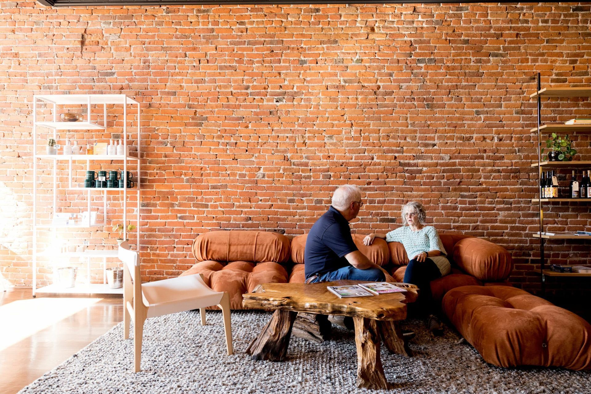 A man and a woman are sitting on a couch in a living room with a brick wall.