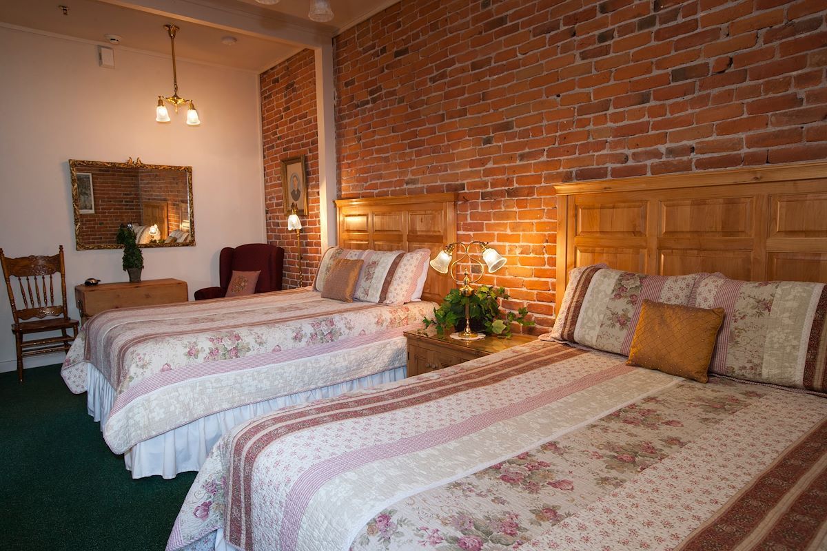 A hotel room with two beds and a brick wall.
