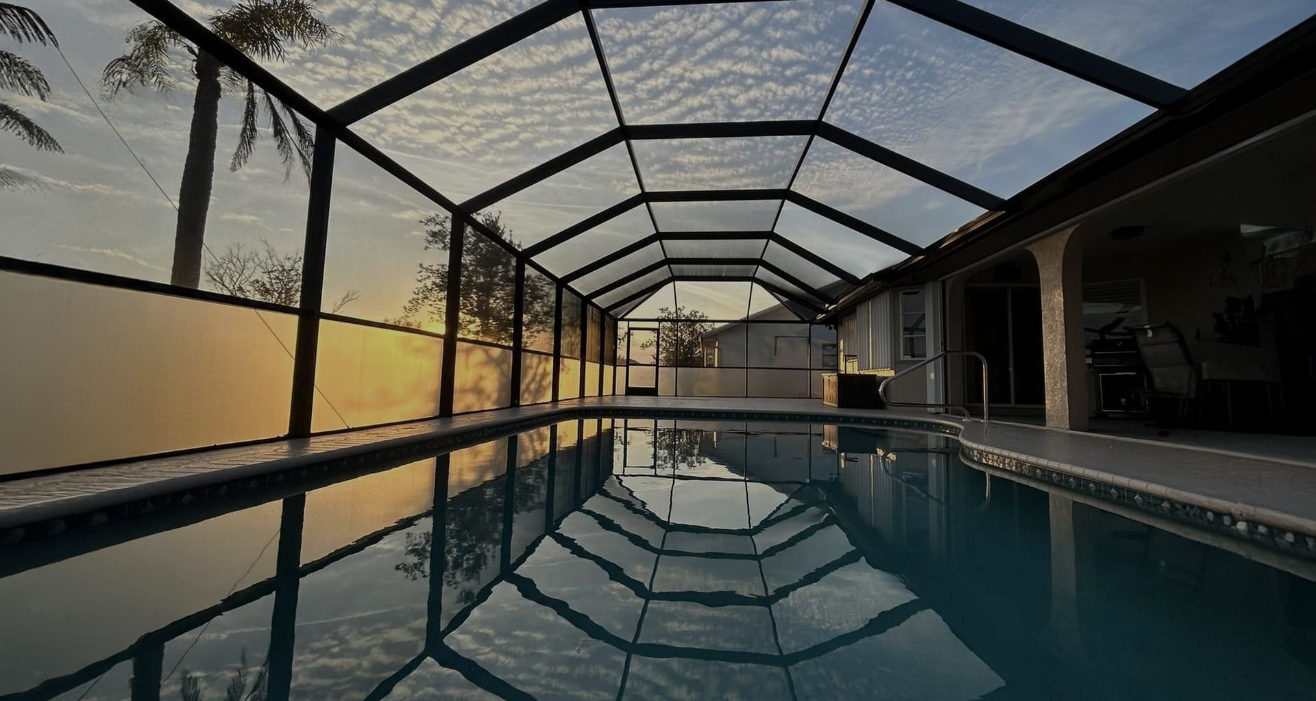 Pool enclosed in a screened-in structure; the water reflects the sky.