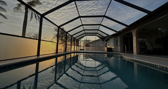 Pool enclosed in a screened-in structure; the water reflects the sky.