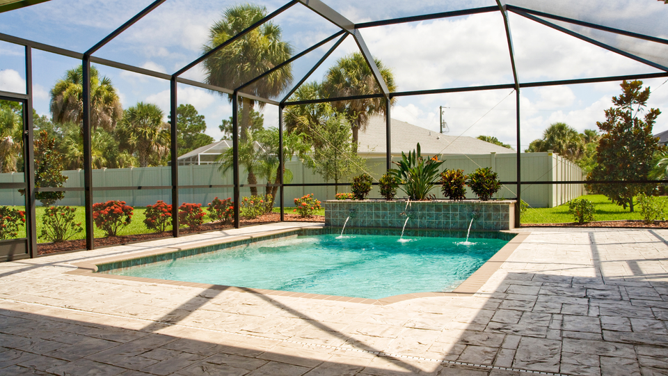 Pool enclosed by a screen with water feature, surrounded by landscaping, and tile patio.