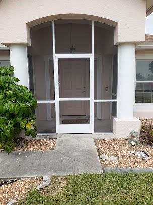 Front entrance with screen door, columns, and pathway leading to the door.