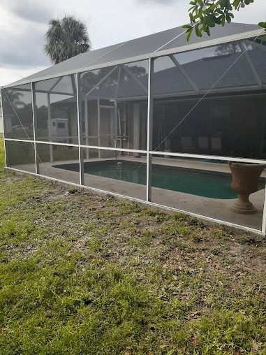 Screened-in pool area with green water, a white frame, and a tall, dark-colored screen.