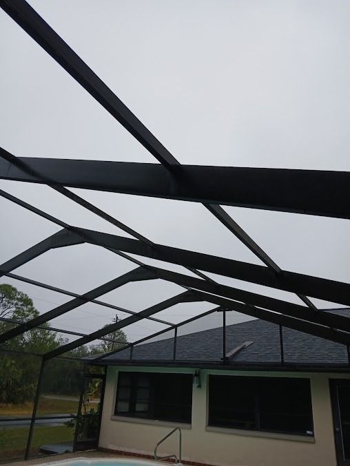 Black framed screen enclosure over a swimming pool, with a gray cloudy sky above.