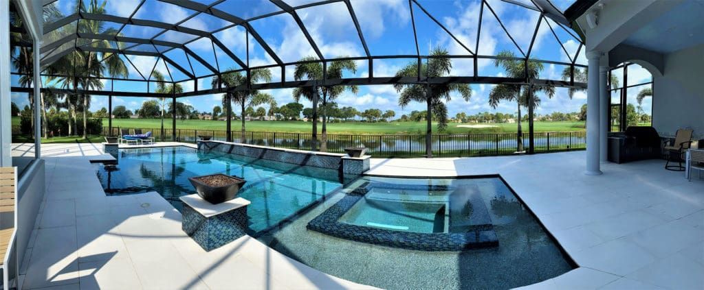 Swimming pool with a view of a golf course framed by palm trees and a blue sky.