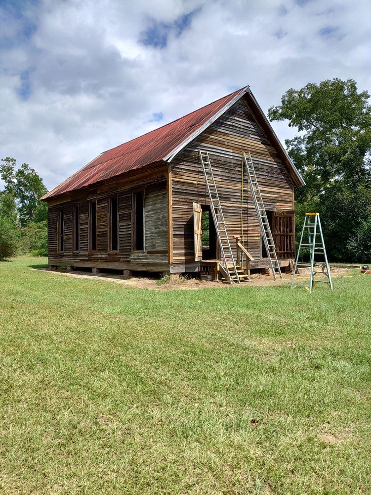 An old wooden building with a red roof is sitting in the middle of a grassy field.