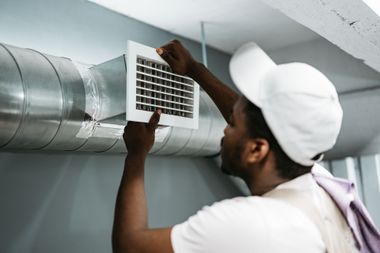 Technician adjusting a wall-mounted air conditioner indoors.