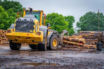A yellow bulldozer is parked in front of a pile of logs.