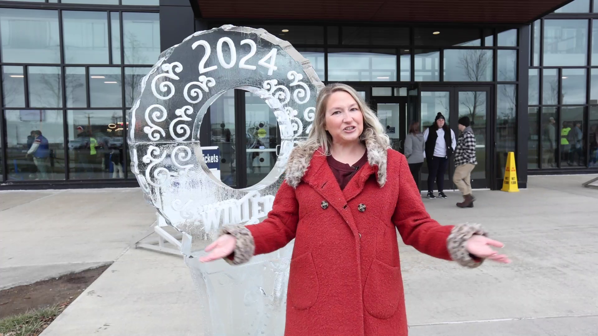 A woman in a red coat is standing in front of a large ice sculpture.