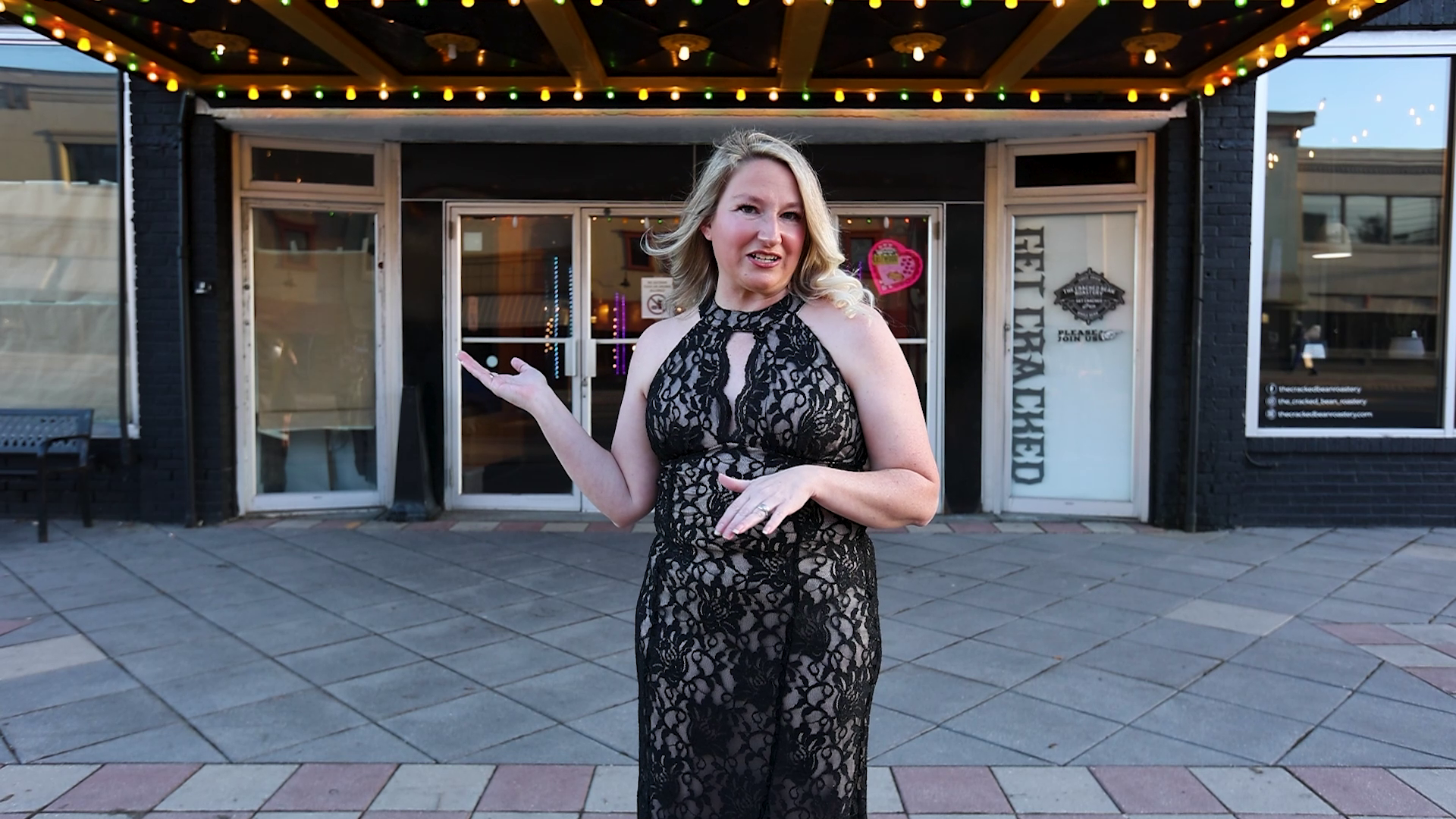 A woman in a black lace dress is standing in front of a building.