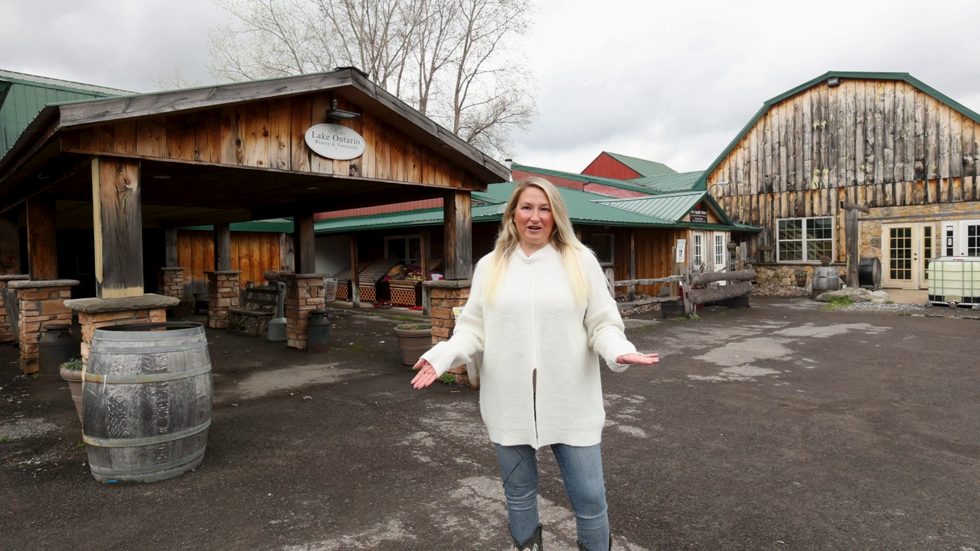 A woman is standing in front of a wooden building with her arms outstretched.