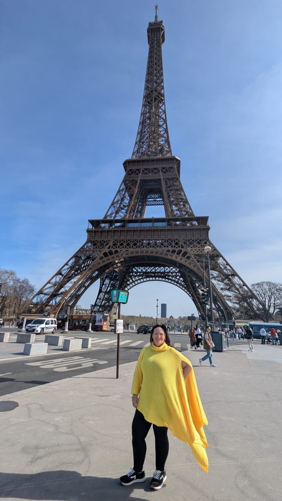 Woman in yellow poncho poses in front of the Eiffel Tower in Paris.