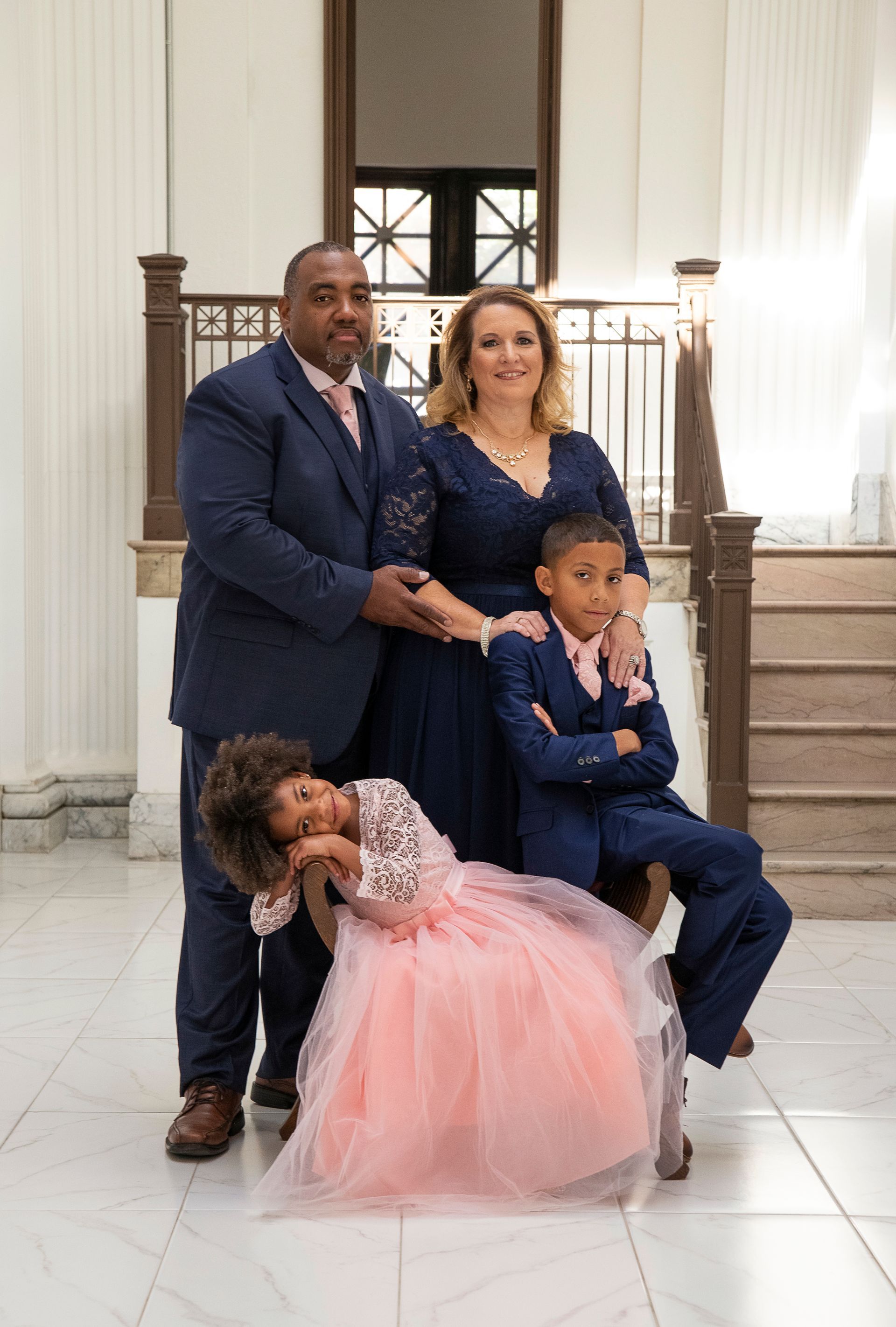 Family of four poses formally in an ornate building. Man and woman stand behind two children.