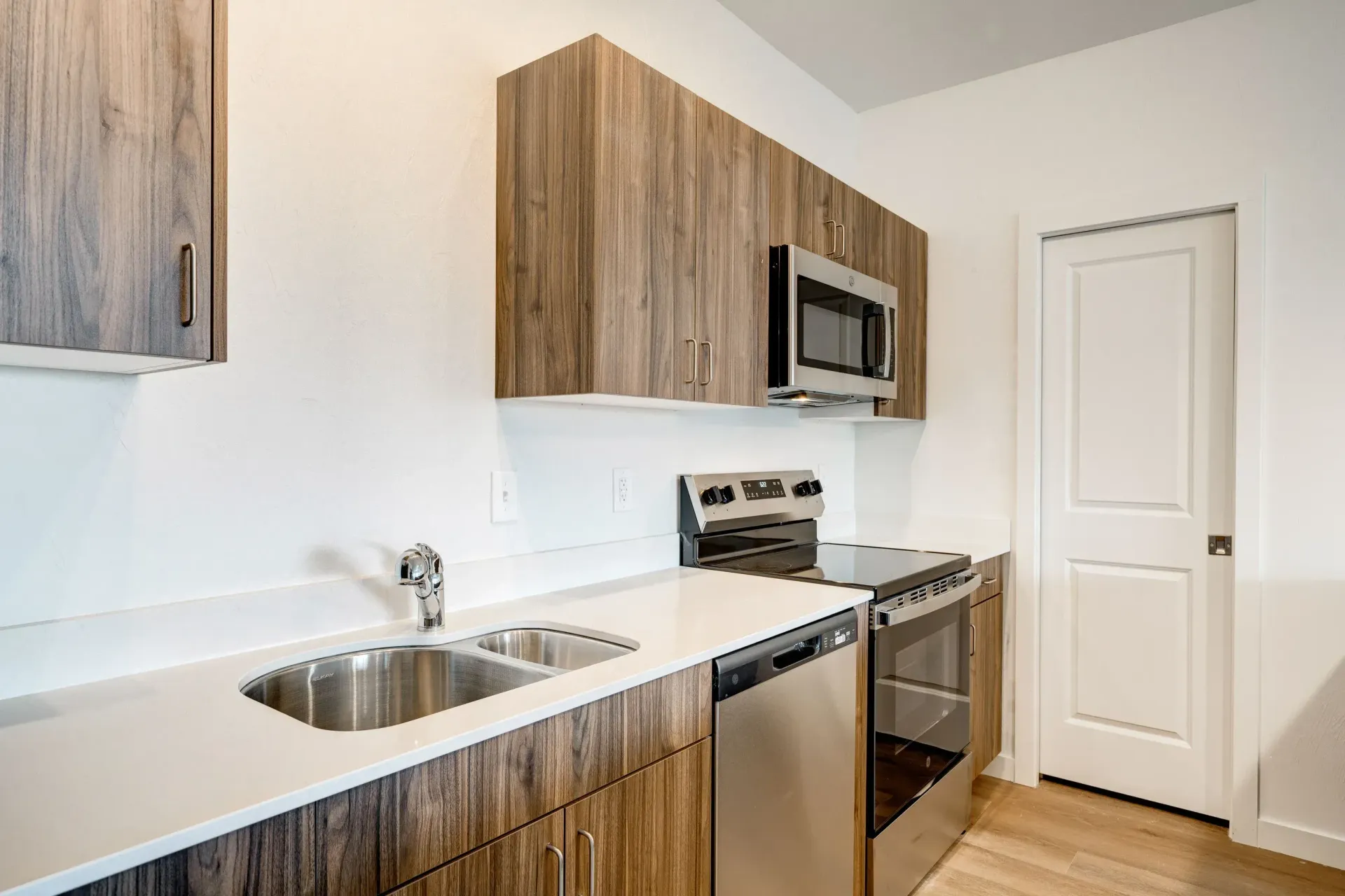 Modern apartment kitchen with woodgrain cabinets, white countertops, and stainless steel appliances.