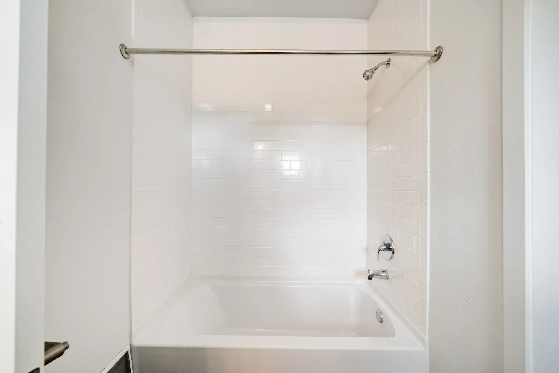 White tile shower/tub in an apartment bathroom with a chrome rod.