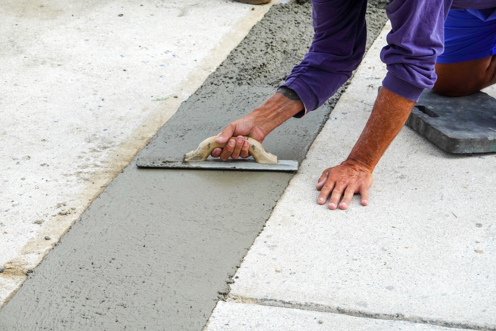A man is laying concrete on the ground with a trowel.