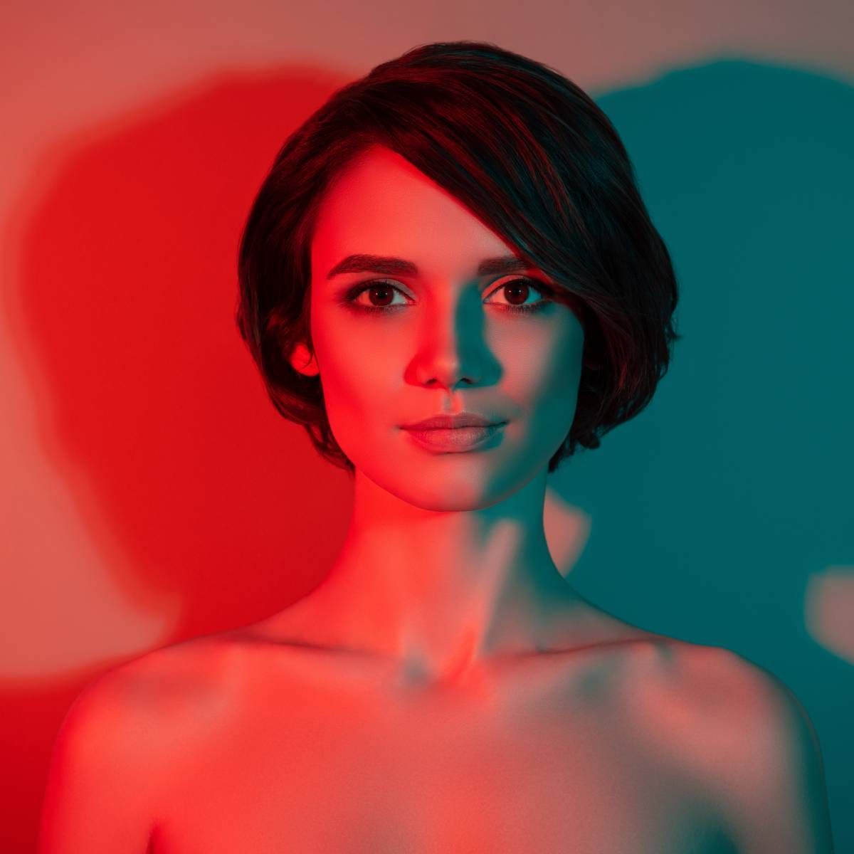 Woman with short hair in red and blue lighting, looking directly at the viewer.