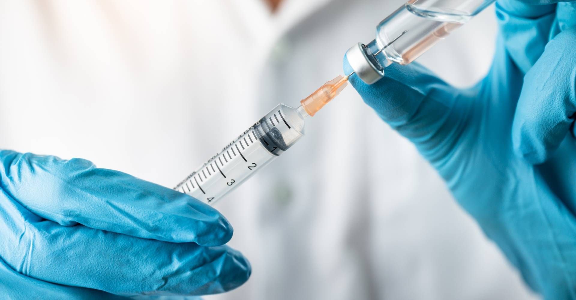 Person wearing blue gloves drawing liquid from a vial into a syringe.