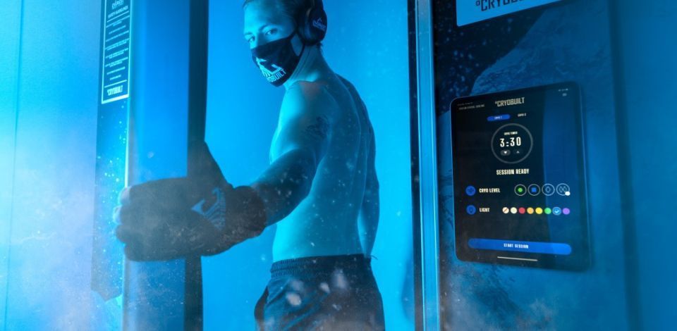 Man in cryotherapy chamber wearing mask and gloves, a touch screen display in view.
