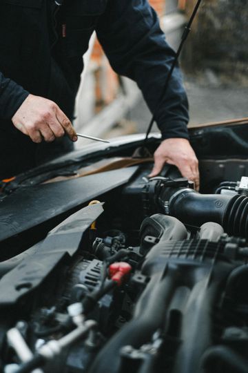 Mechanic working on a car engine, hands visible, outdoors.