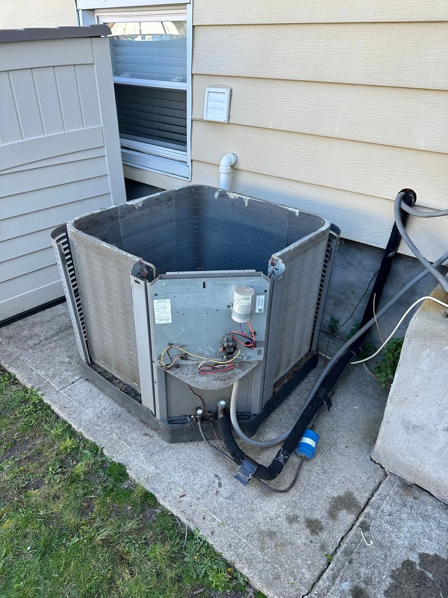 Outdoor air conditioning unit against a beige wall, on a concrete slab.