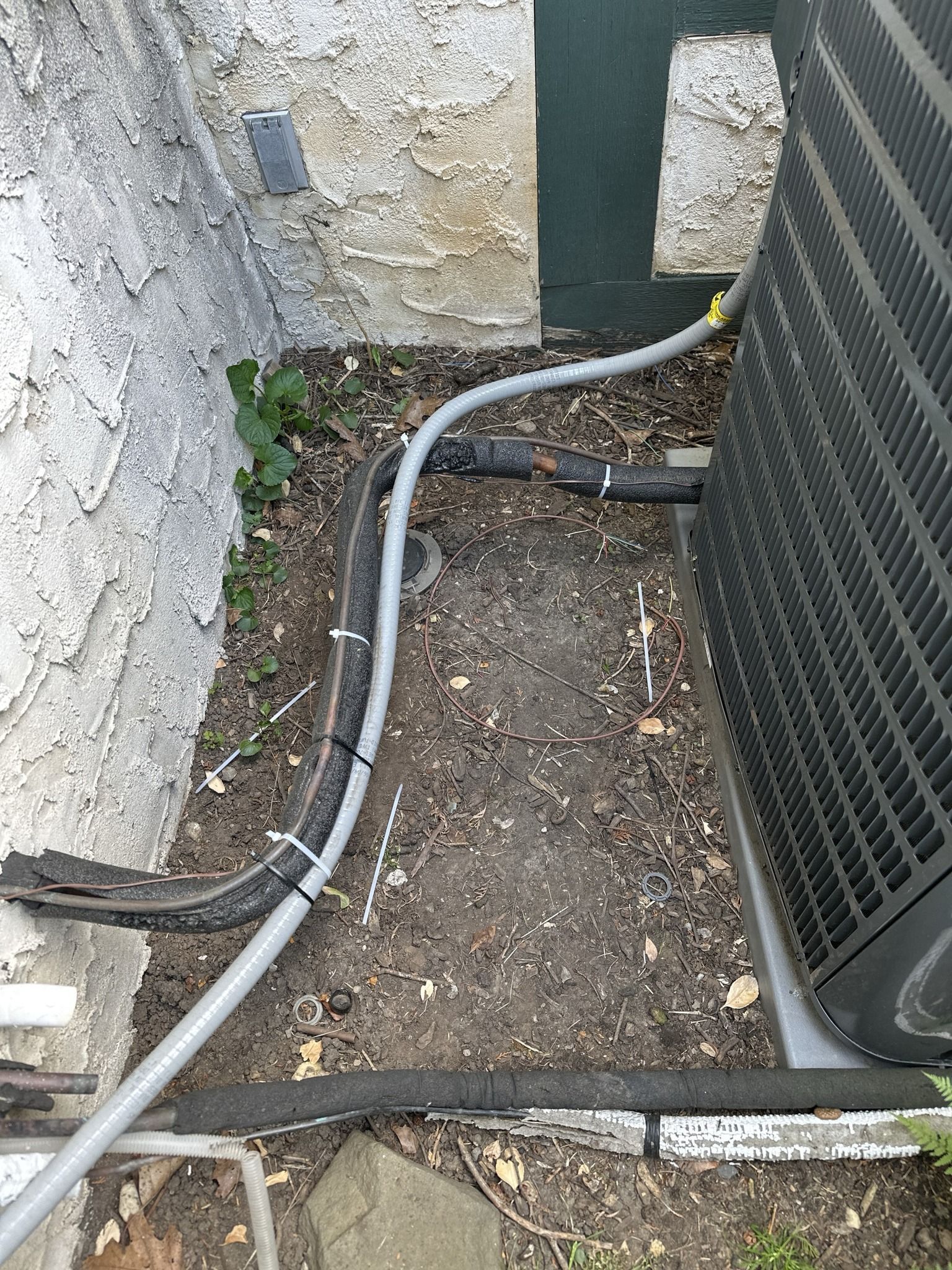 AC unit set into a small recess against a light stucco wall; gray conduit and ground cover.