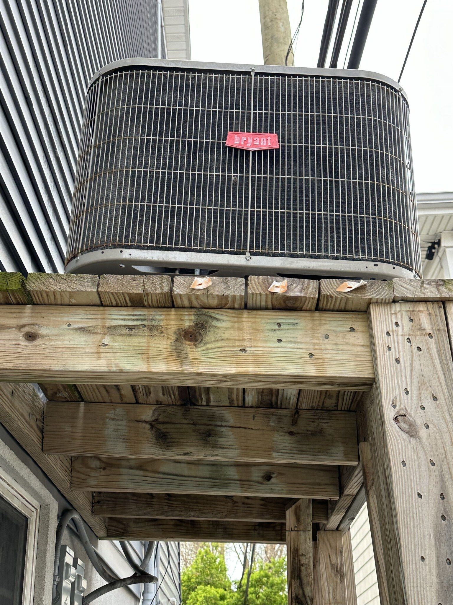 Air conditioner on a weathered wooden deck; gray siding in background.