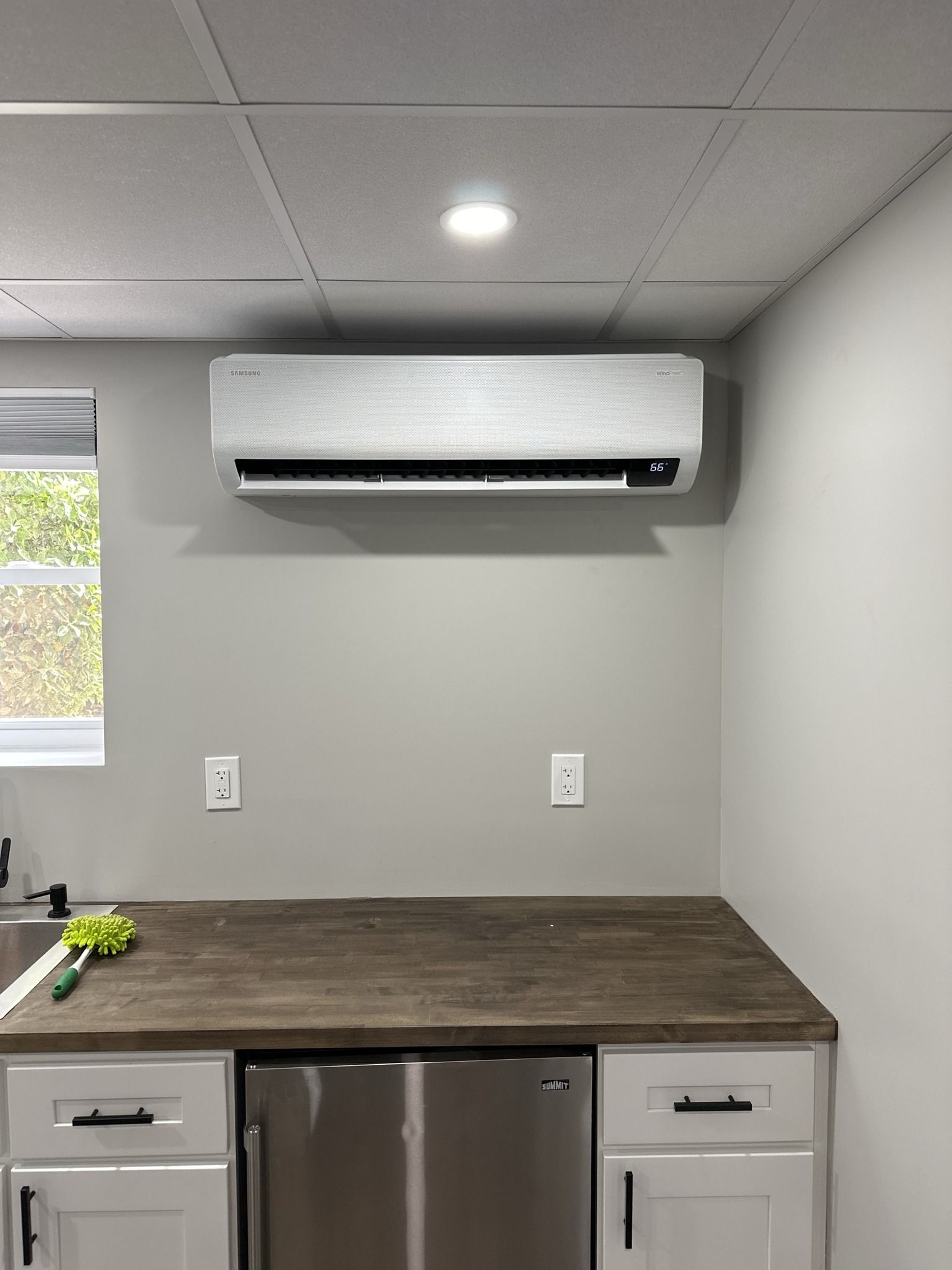 A kitchen with a stainless steel refrigerator and a wall mounted air conditioner.