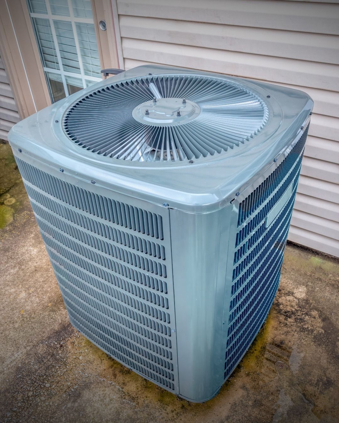 Gray air conditioning unit outside a house, next to a door.