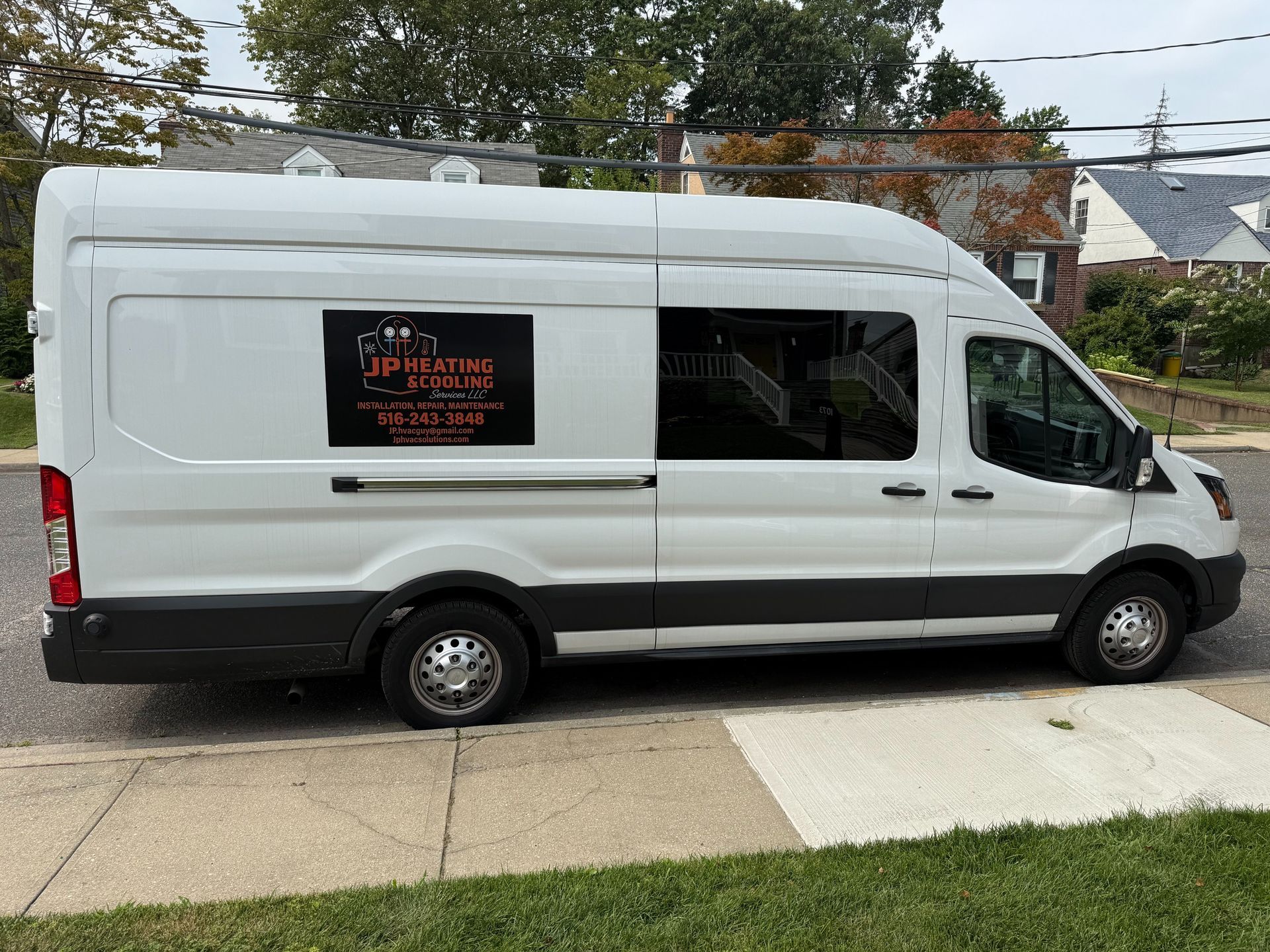 White van parked on a street with a sign on the side. Houses and green grass in the background.