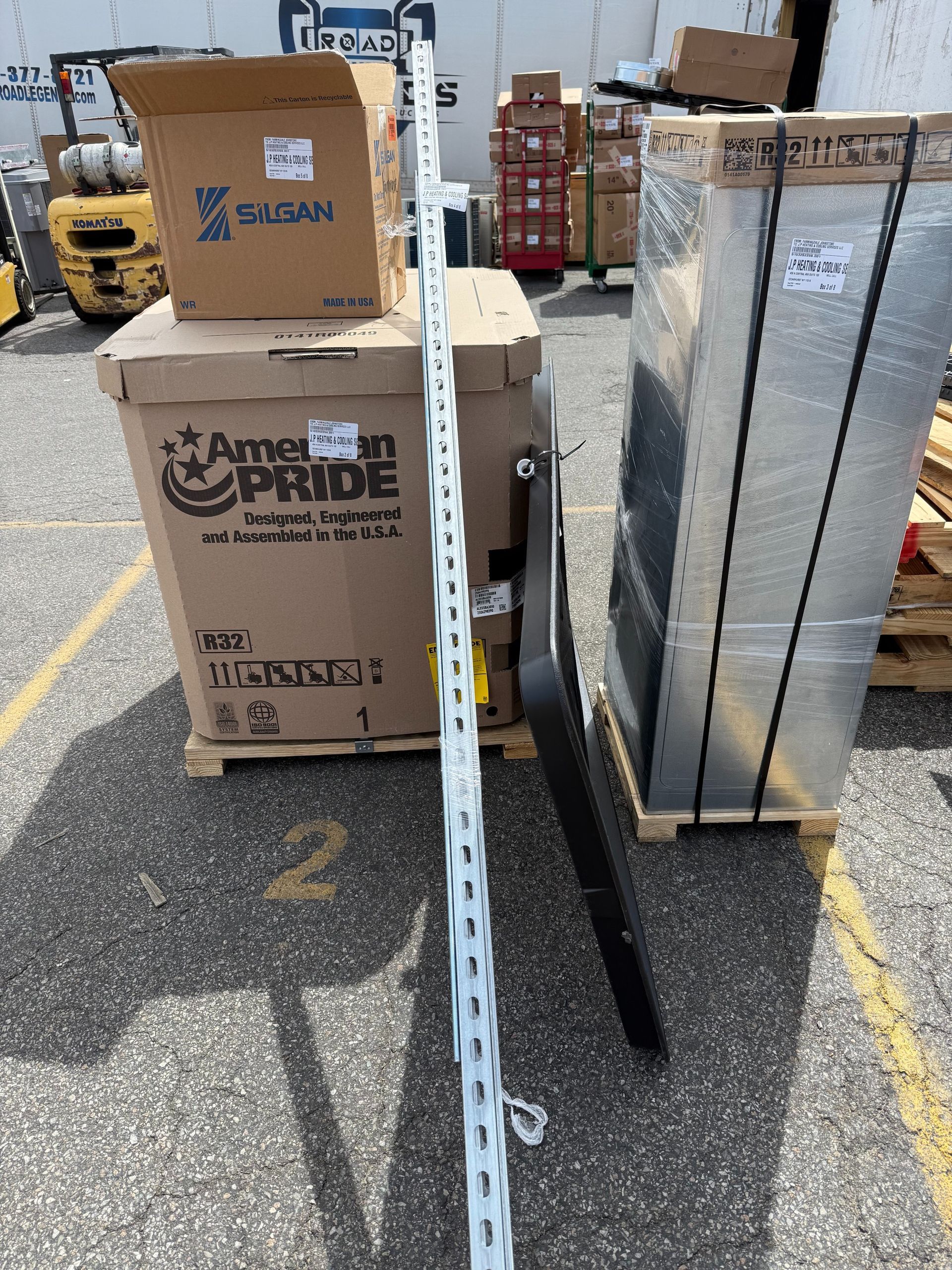 Boxes on pallets with a long metal rail and forklift forks on asphalt.