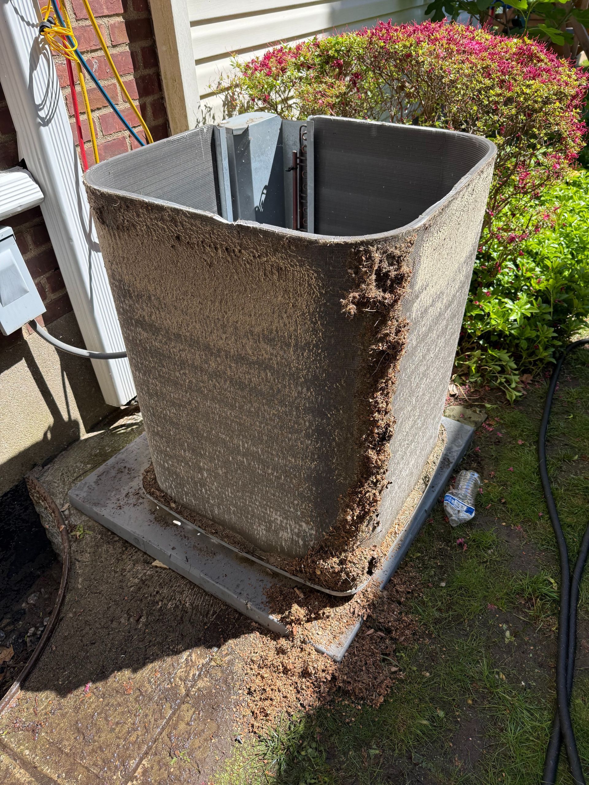 An air conditioner unit with a crumbling, dirty surface, placed outside near greenery.